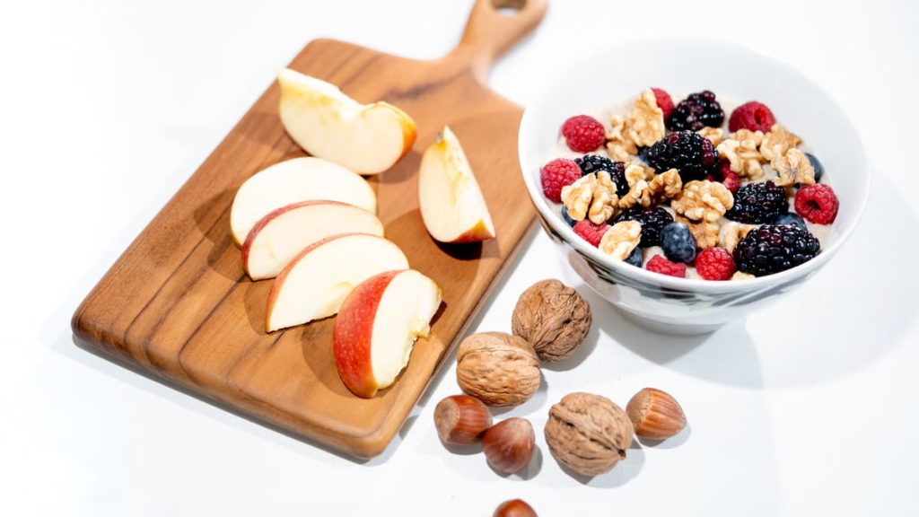 A vibrant breakfast bowl with mixed berries, walnuts, and apple slices on a rustic board.